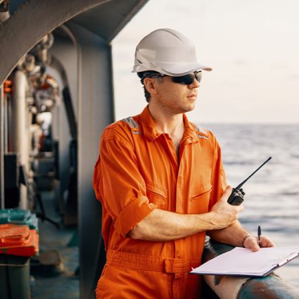 Deck Officer on deck of offshore vessel holds VHF walkie-talkie radio