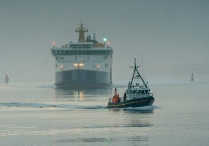 Fishing boat guiding ferry through coastal fog