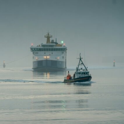 Fishing boat guiding ferry through coastal fog