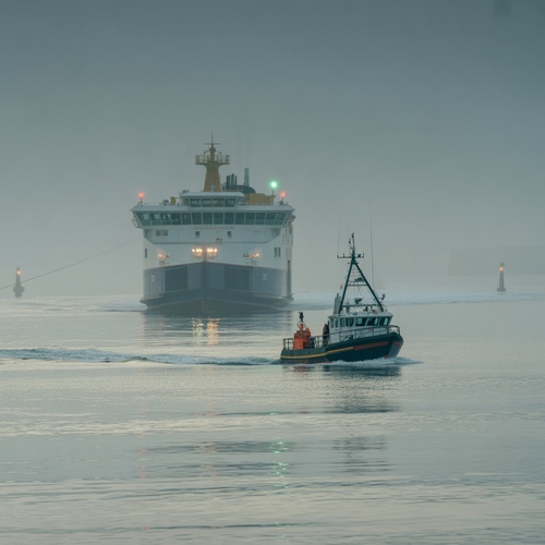 Fishing boat guiding ferry through coastal fog